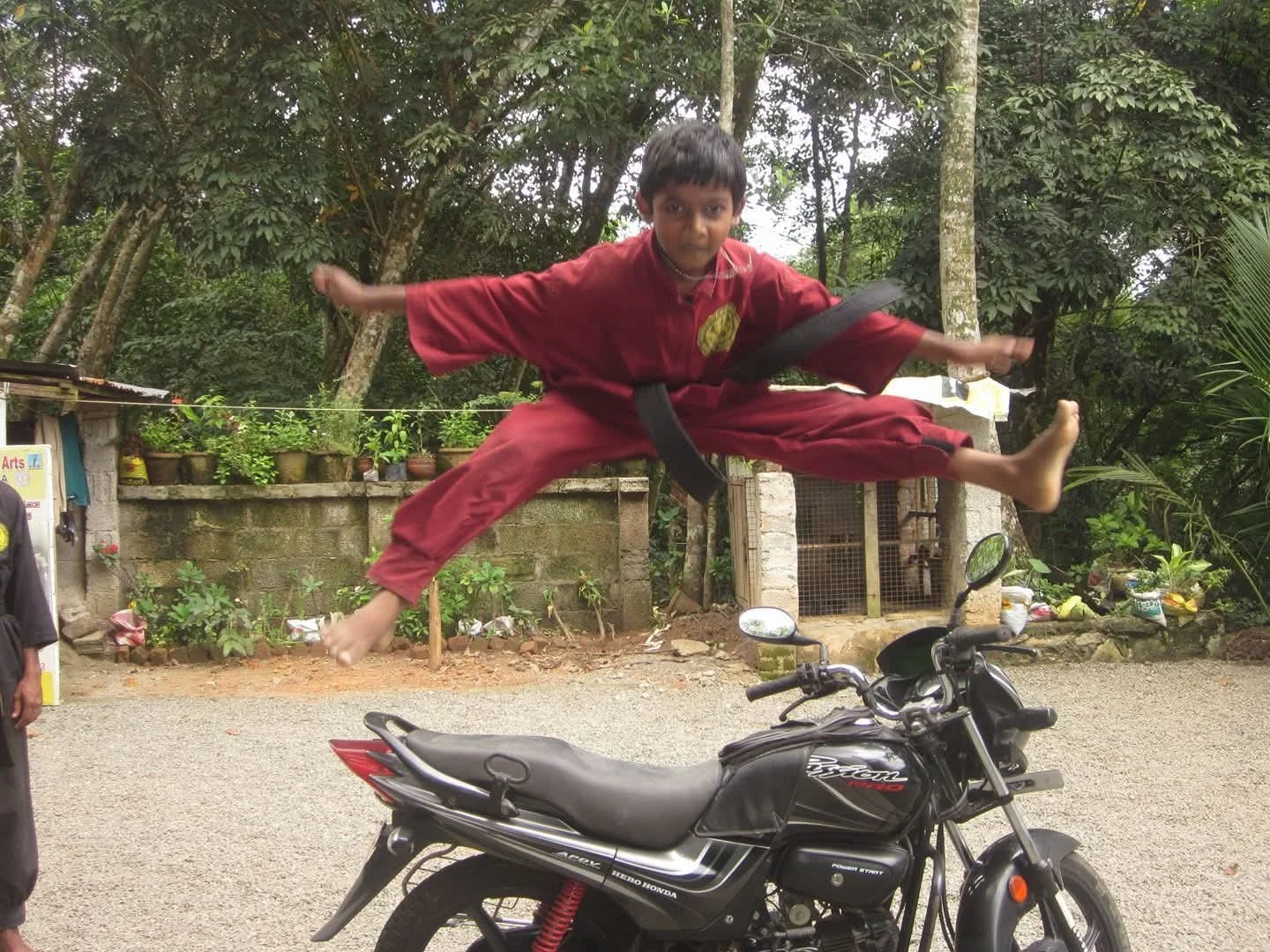 A young martial arts student demonstrates an aerial split under supervision